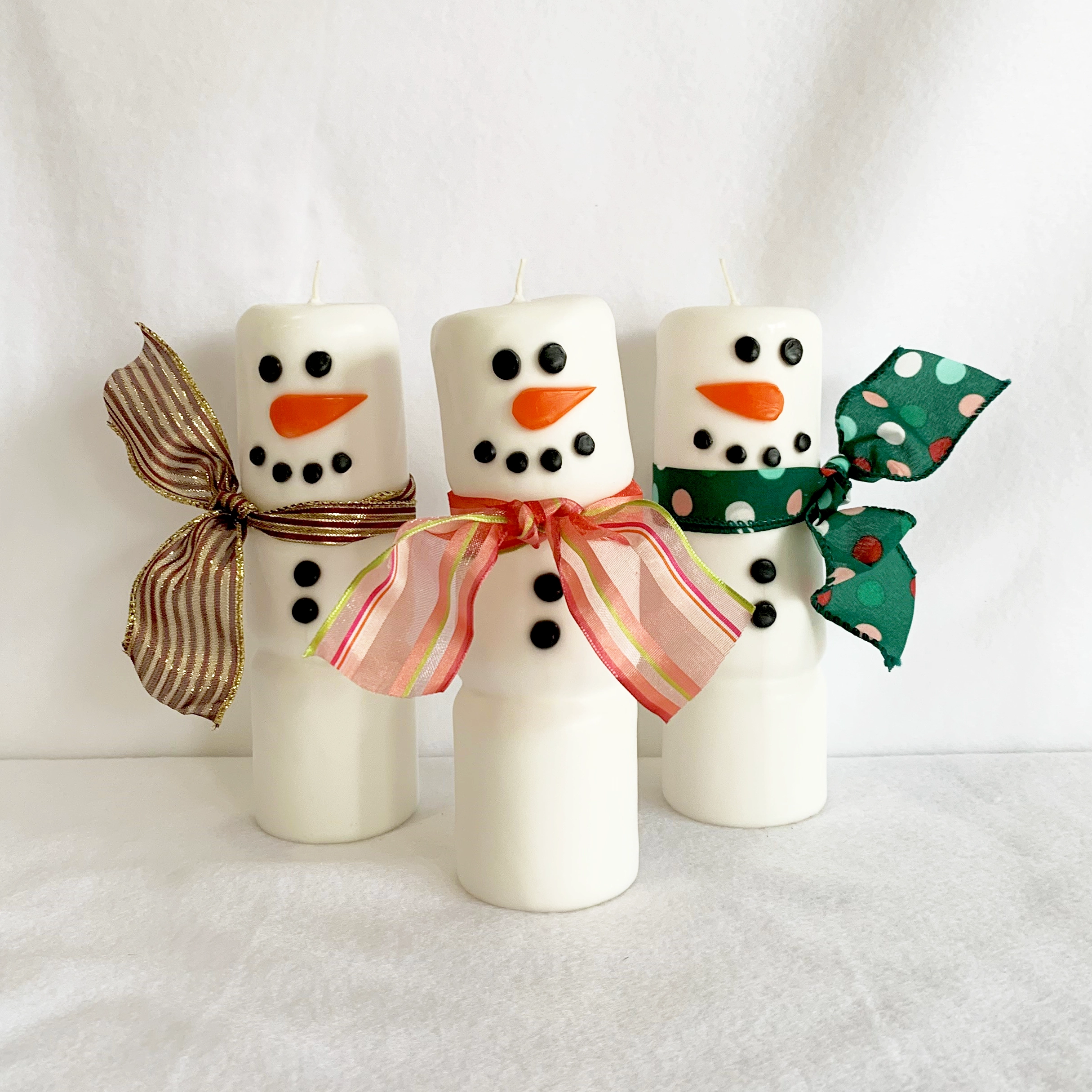 Three snowmen column candles with colorful ribbon scarves.